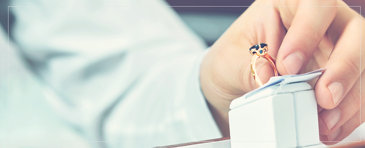 Man holding a yellow gold solitaire emerald engagement ring at a showcase display.