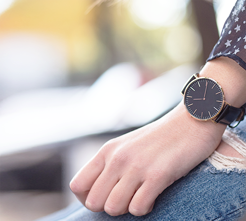 Woman’s wrist featuring a yellow gold watch with a black dial and black leather strap.