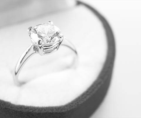 White gold solitaire diamond engagement ring in a round ring box.