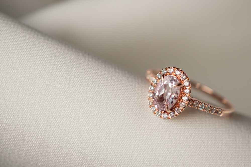 Rose gold engagement ring centered with a pink diamond surrounded by a white diamond halo and white diamonds in the band.