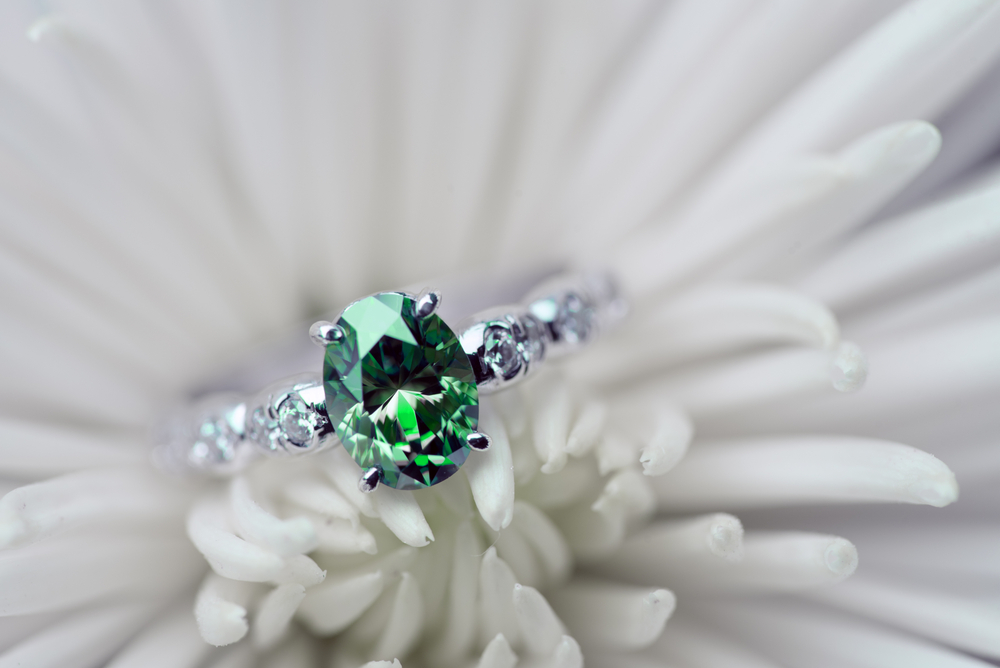 White gold engagement ring centered with a green diamond and white diamonds in the band.