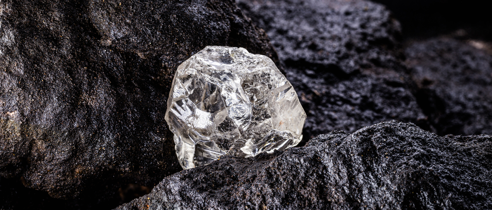 Rough uncut diamond on black rocks.