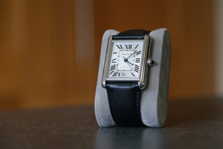Cartier Tank watch with leather strap on white display.