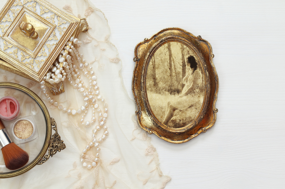 Pearl strand necklaces coming out of antique jewelry box next to antique framed photo.