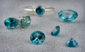 Loose cut blue zircon and white gold ring centered with blue zircon on a white table.