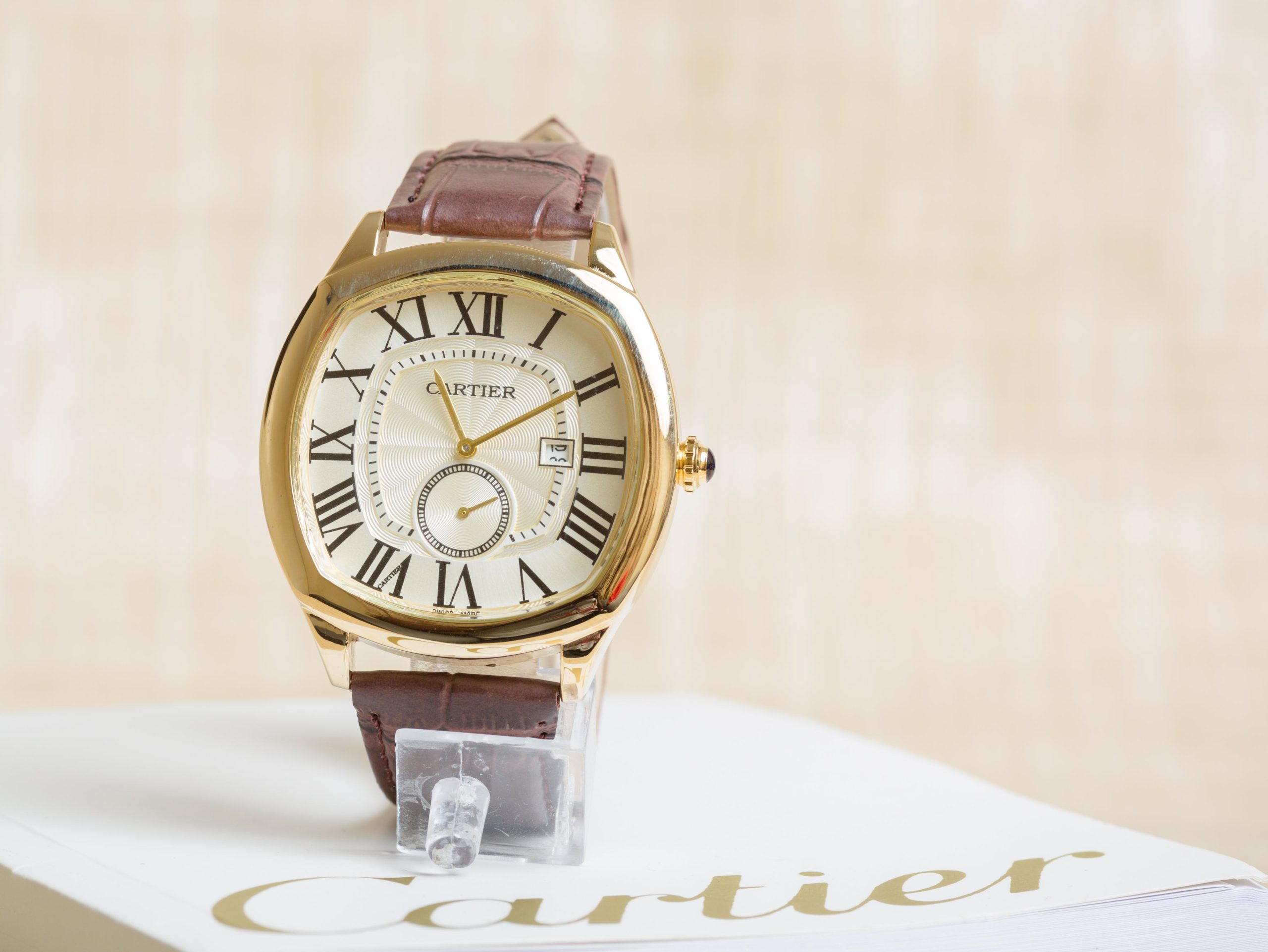 Yellow gold Cartier with white Roman numeral dial and brown leather strap.