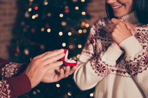 Man proposing to woman in front of Christmas tree.