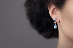 Woman's ear with blue topaz and diamond dangle earrings
