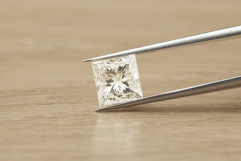 Loose princess cut diamond held by tweezer.