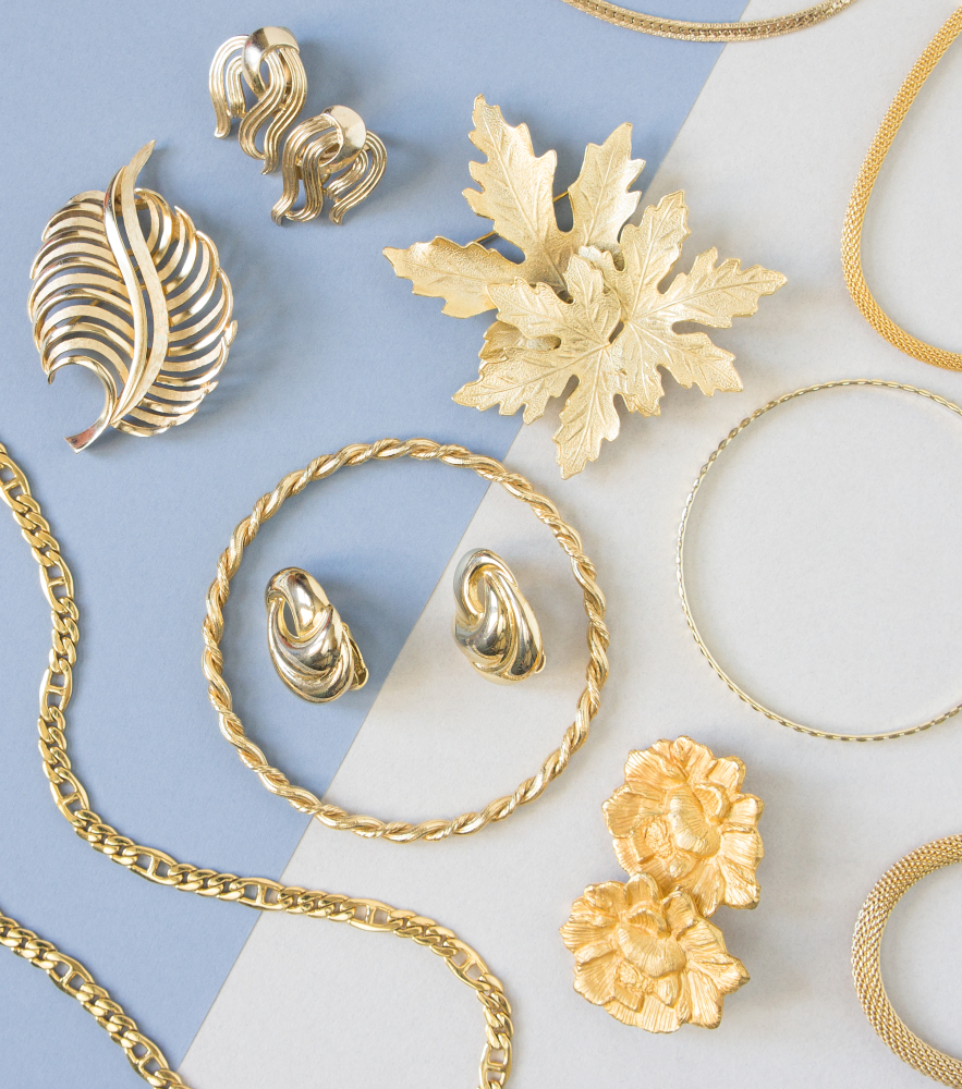 Vintage yellow gold earrings, bracelets, and necklaces on a blue and white background.