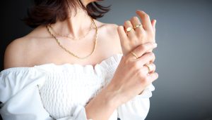 Woman in white shirt with yellow gold necklace and yellow gold rings on both hands.