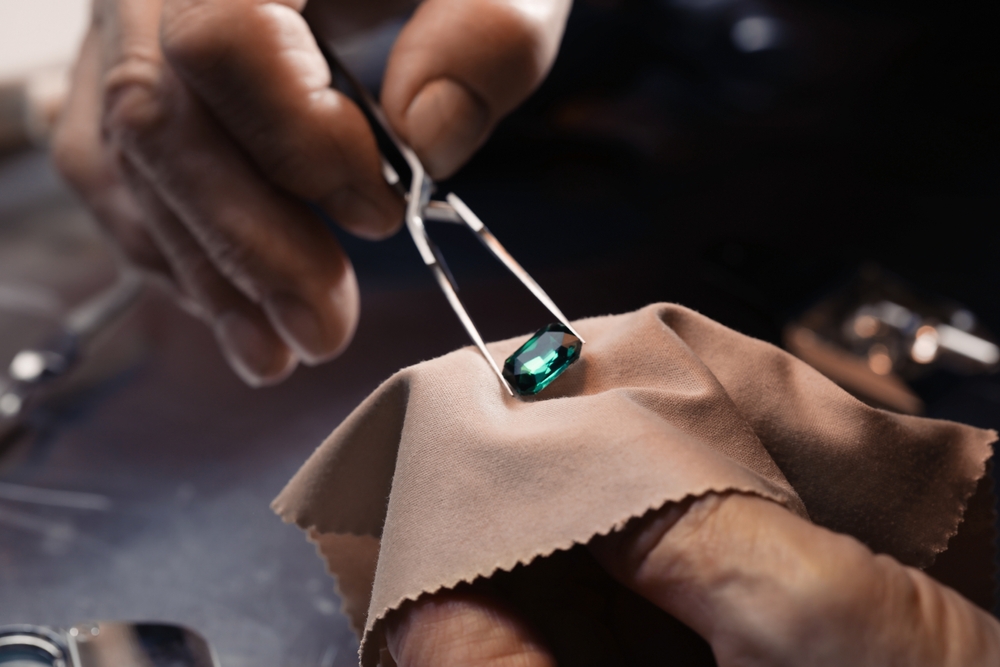Jeweler holding round cut green gemstone with tweezers.