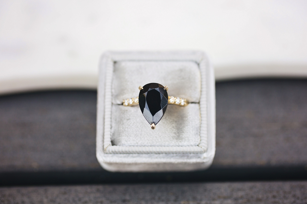 Yellow gold engagement ring centered with a pear cut black diamond and white diamonds in the band.