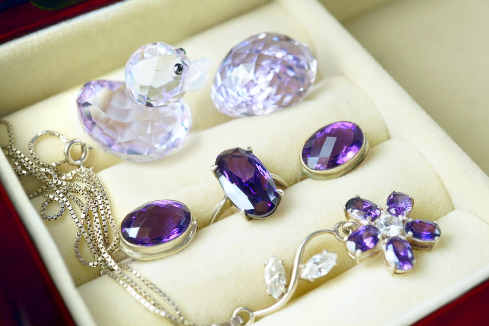 Loose oval cut amethyst in jewelry storage box with whtie gold amethyst rings and necklace.