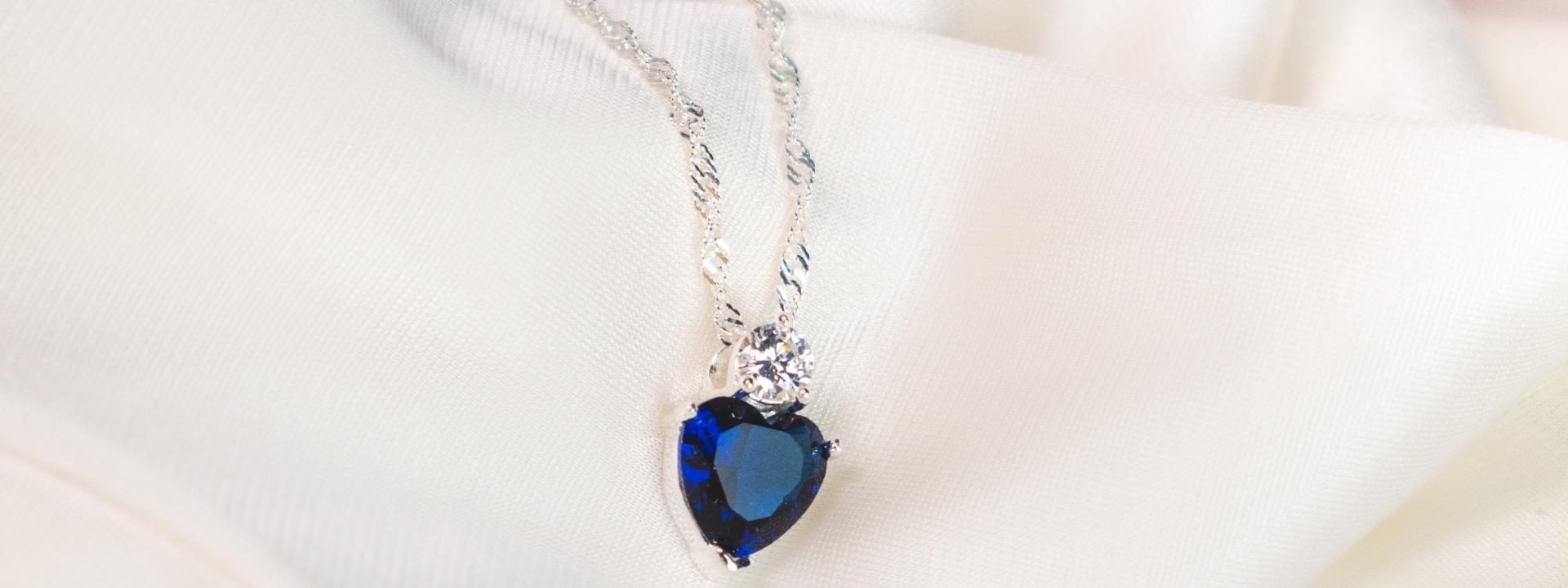 White gold necklace centered with a heart cut blue sapphire and round cut diamond on a diamond cut chain.