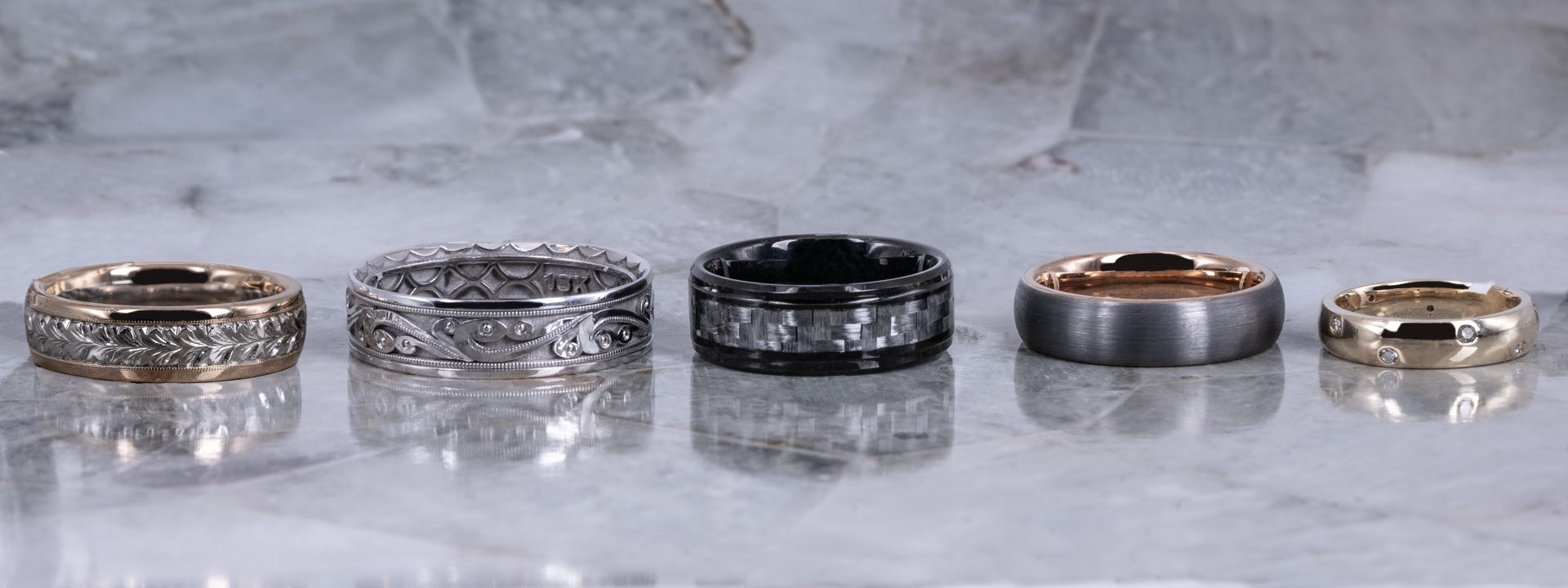 Five various men's wedding bands on marble background.