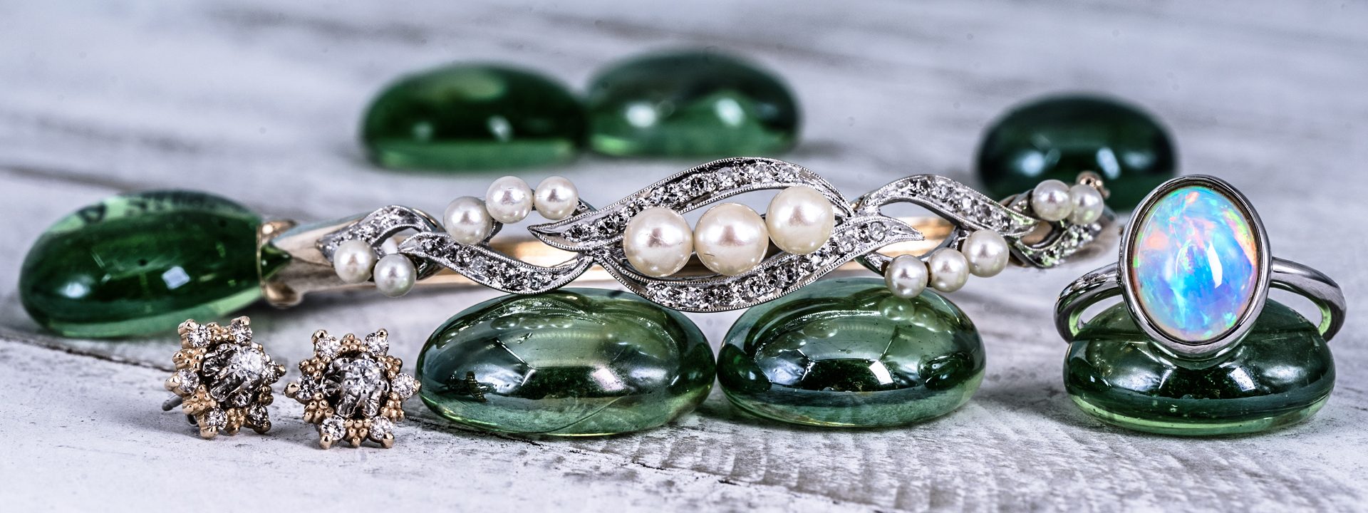 Opal ring, pearl and diamond bangle, and chocolate and white diamond earrings laid on green beads.