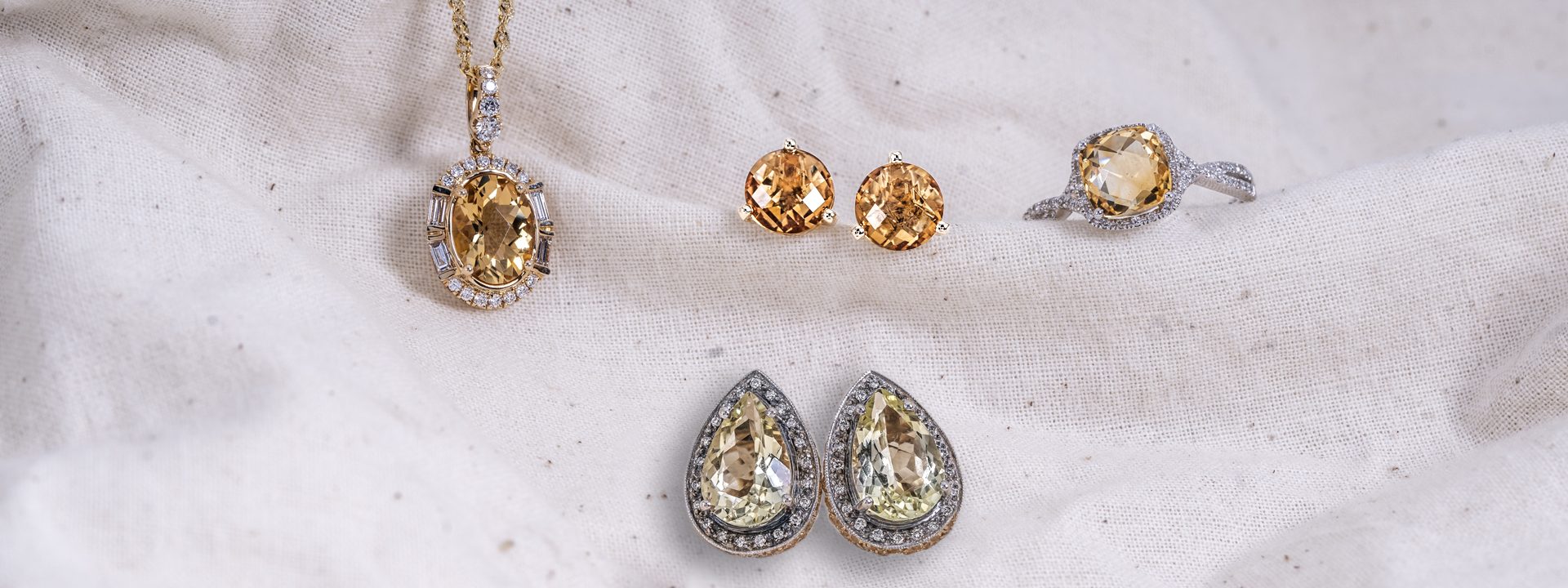 Two pairs of citrine stud earrings, one citrine ring, and one citrine pendant necklace on a white cloth background.