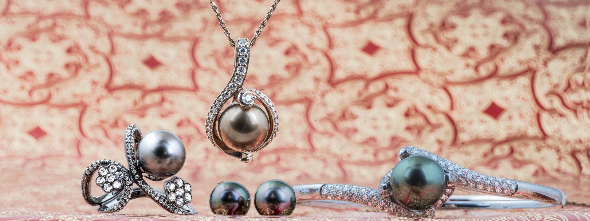 Pearl bangle, stud earrings, ring, and pendant necklace in front of regal textured background.