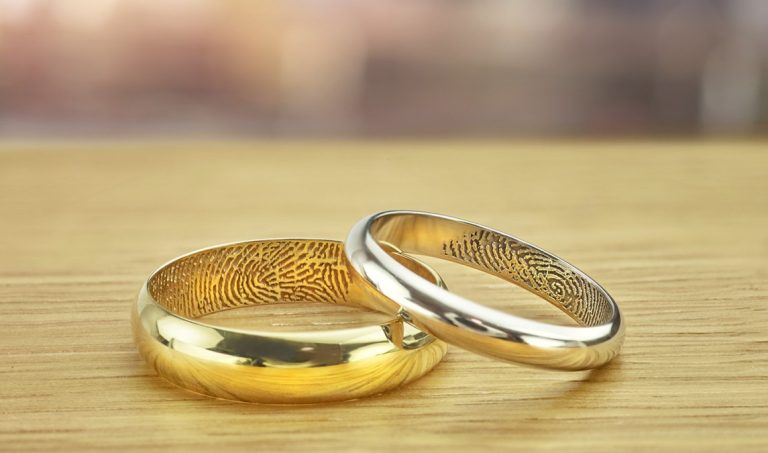 Two yellow gold engraved wedding bands on a wooden table.