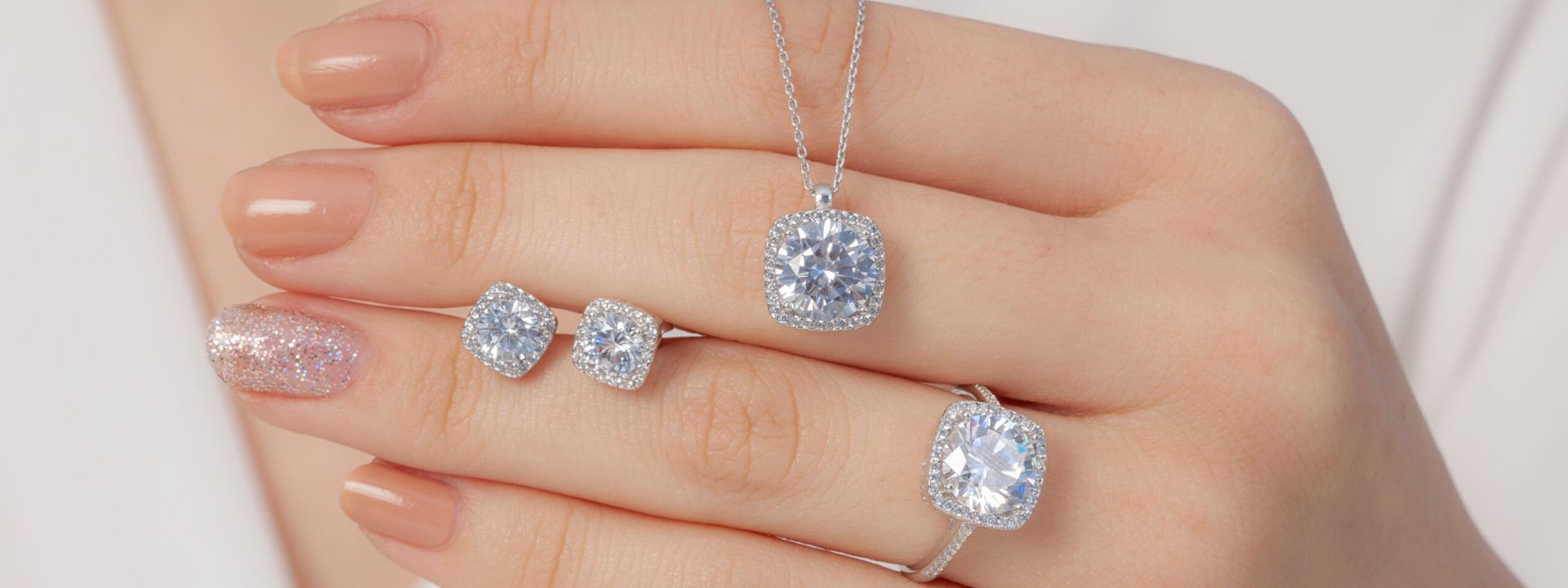 Woman's hand featuring diamond stud earrings, diamond engagement ring, and diamond pendant necklace.