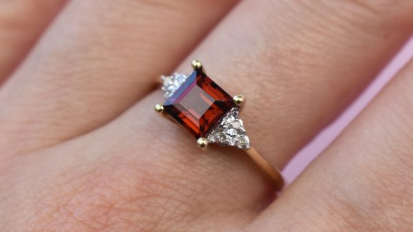 Yellow gold three-stone ring centered with a garnet and two diamond side-stones.
