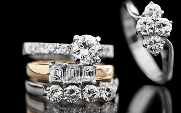 Stacks of diamond engagement rings in various styles including three-stone, solitaire, and cluster settings.