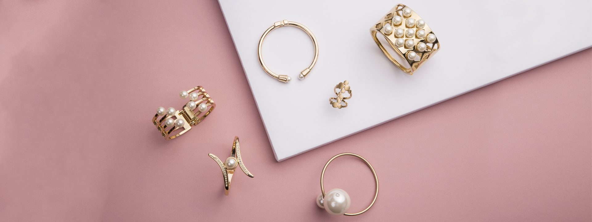 Various dainty yellow gold jewelry pieces on a pink background.